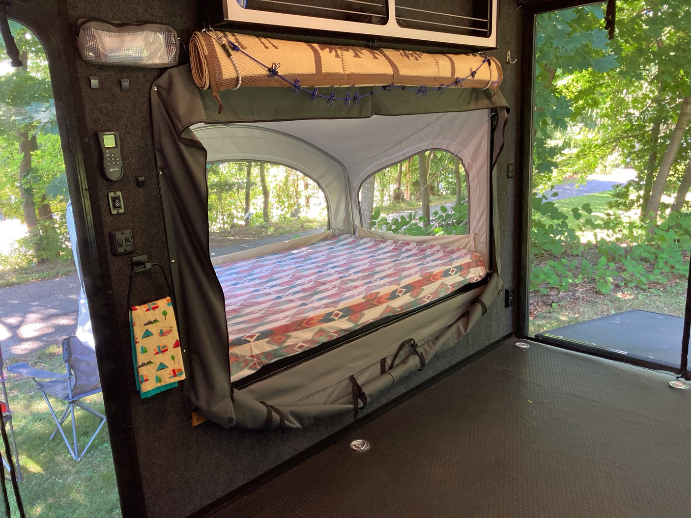 RV rental interior: A comfy pop-out bed with colorful blanket and big windows showing lush outdoor scenery.