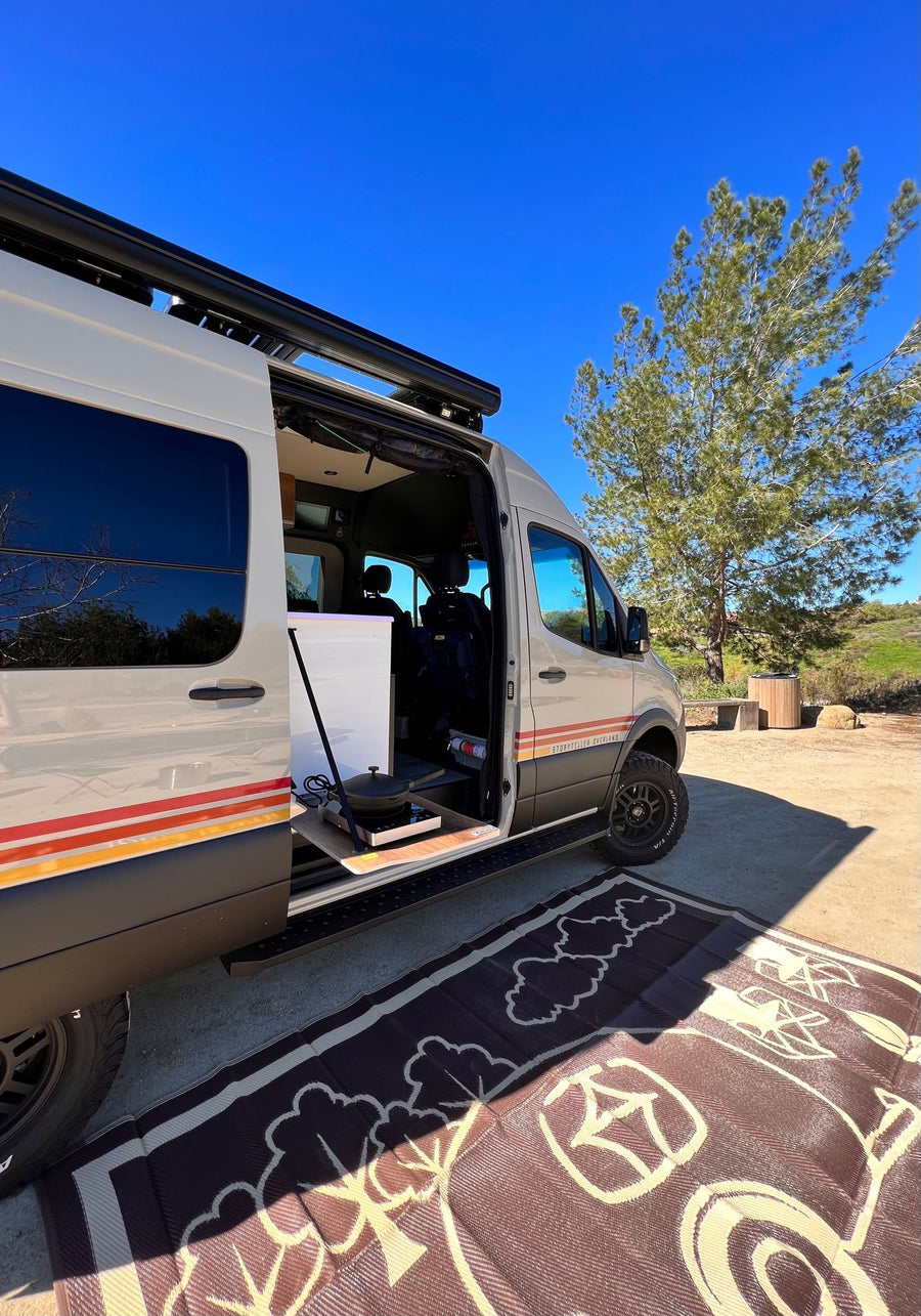 This RV rental, a Storyteller Overland van, is set up for van life with an outdoor kitchen and mat.