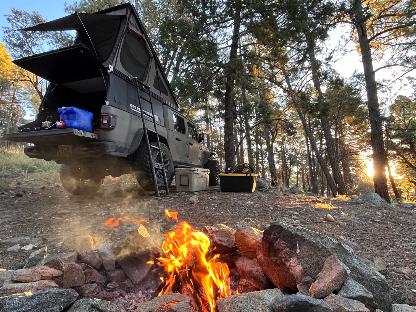 Overlanding setup: Jeep Gladiator with rooftop tent, campfire. A perfect RV rental alternative for forest adventures.