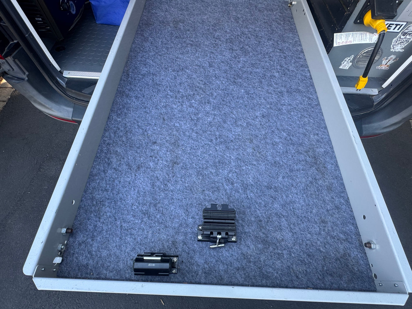 RV rental van's pull-out cargo slide, carpeted and equipped with two black securing clamps, for efficient gear storage.