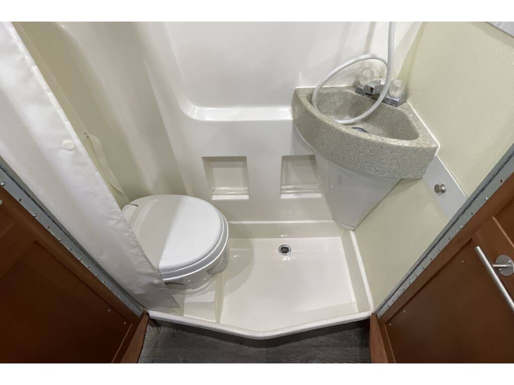 Compact RV rental bathroom with a white toilet, corner sink, and shower pan with curtain.