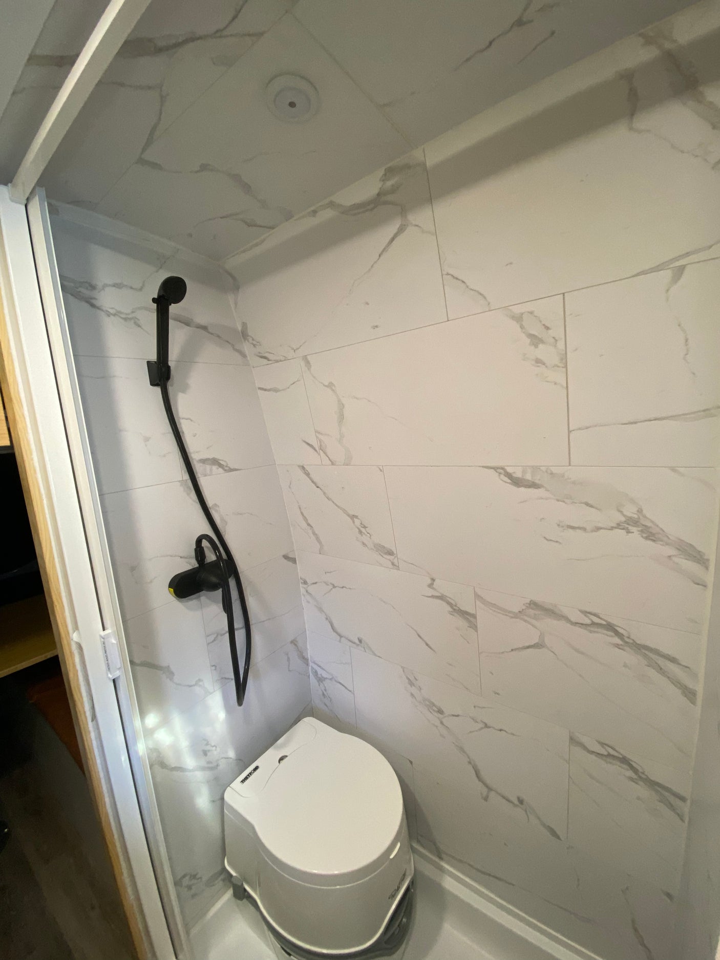 RV rental: Bright, compact bathroom with white marbled walls, black shower head, and white portable toilet.