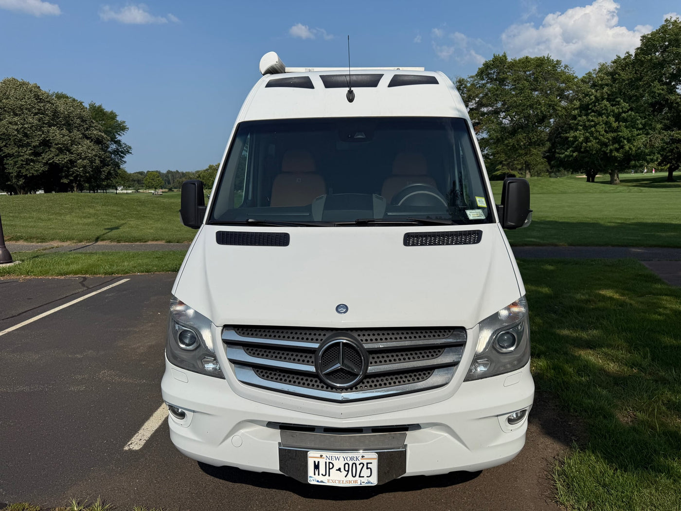parked on a sunny day with a green park/golf course background. NY plate MJP-9025.|RV rental exterior: white shower access panel with lock — photo 8