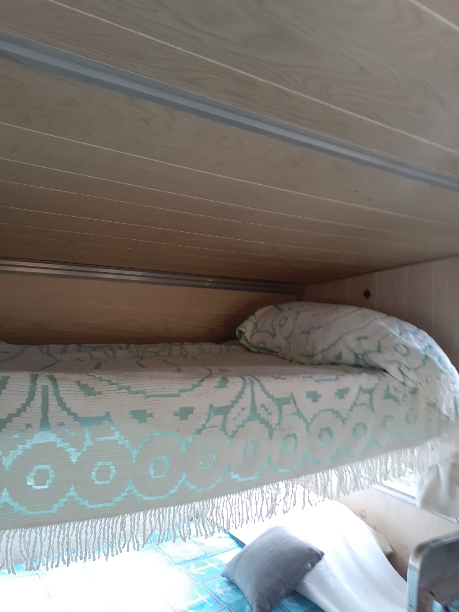 Cozy RV rental interior featuring light wood paneling, a white and teal patterned blanket, and a comfy bed.
