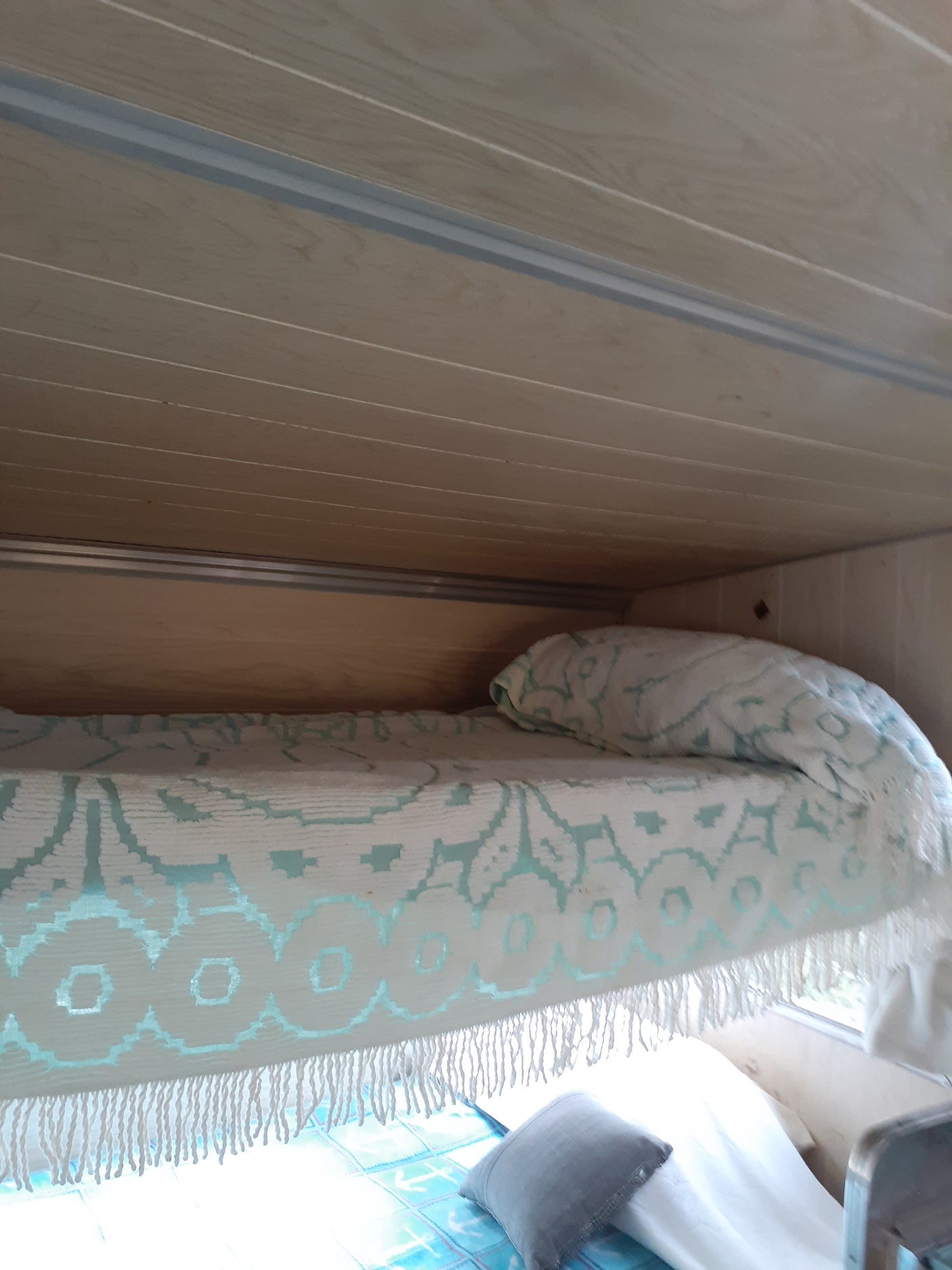 Cozy RV rental interior featuring light wood paneling, a white and teal patterned blanket, and a comfy bed.
