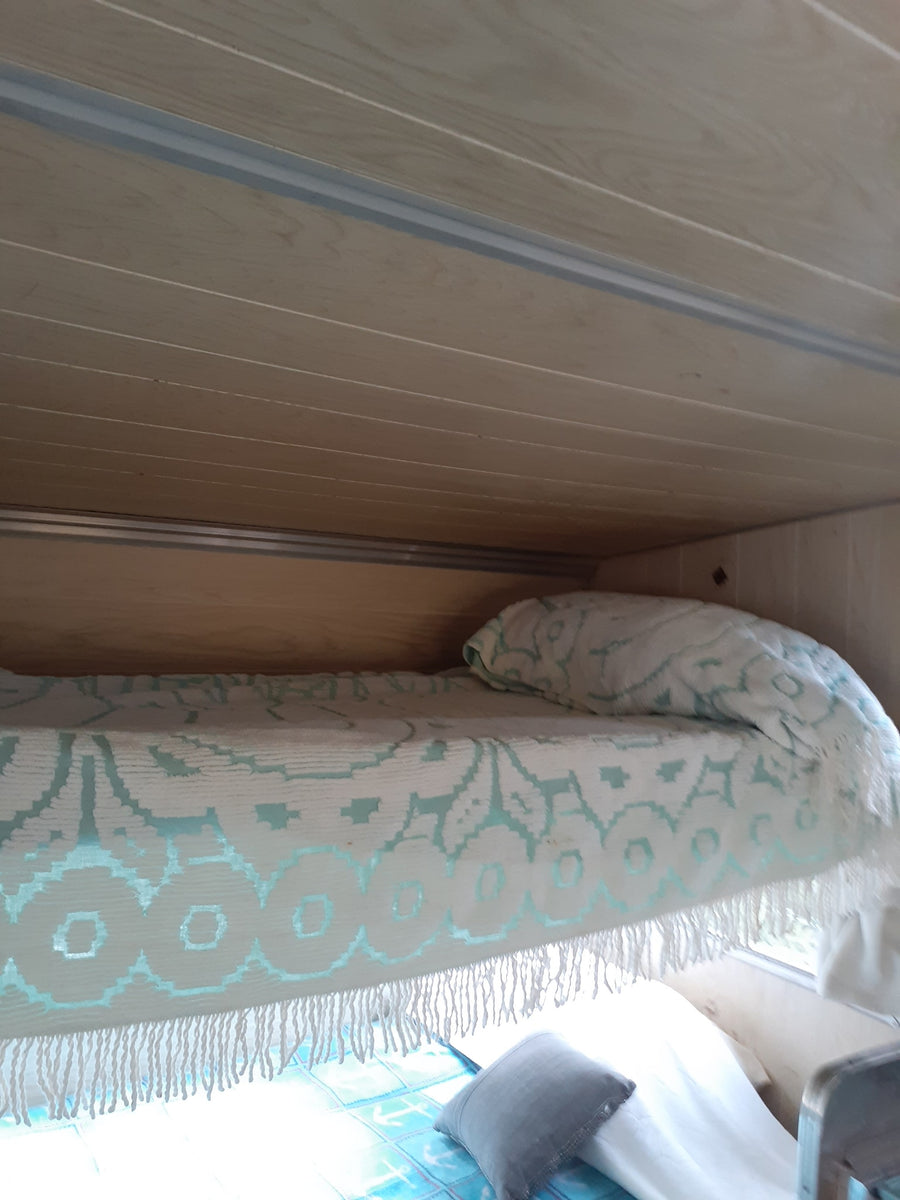 Cozy RV rental interior featuring light wood paneling, a white and teal patterned blanket, and a comfy bed.