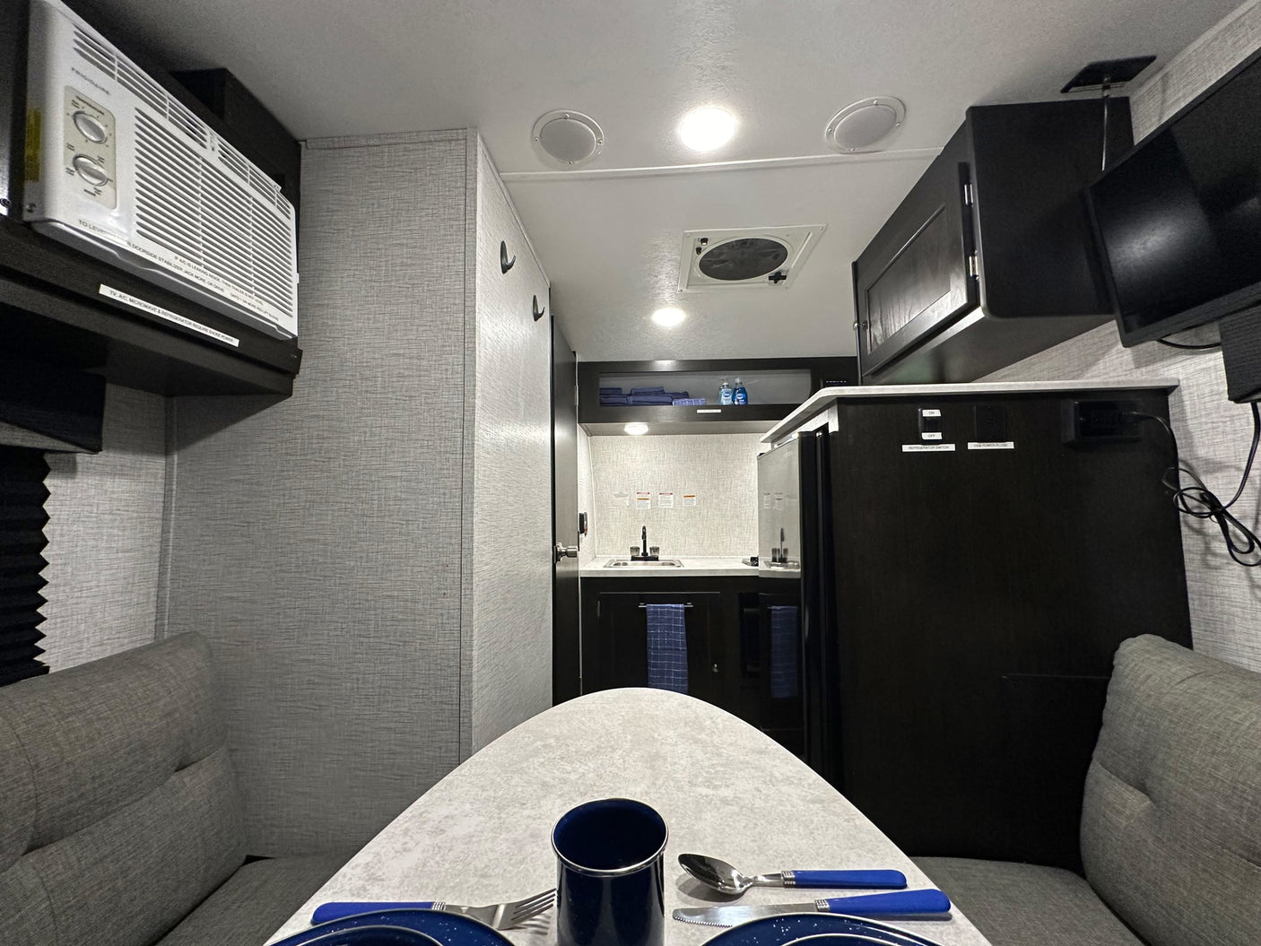Inside a modern rv rental: dining table setup, compact kitchen, AC unit, and entertainment for a comfortable journey.