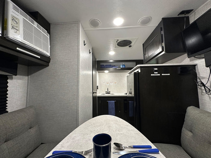 Inside a modern rv rental: dining table setup, compact kitchen, AC unit, and entertainment for a comfortable journey.