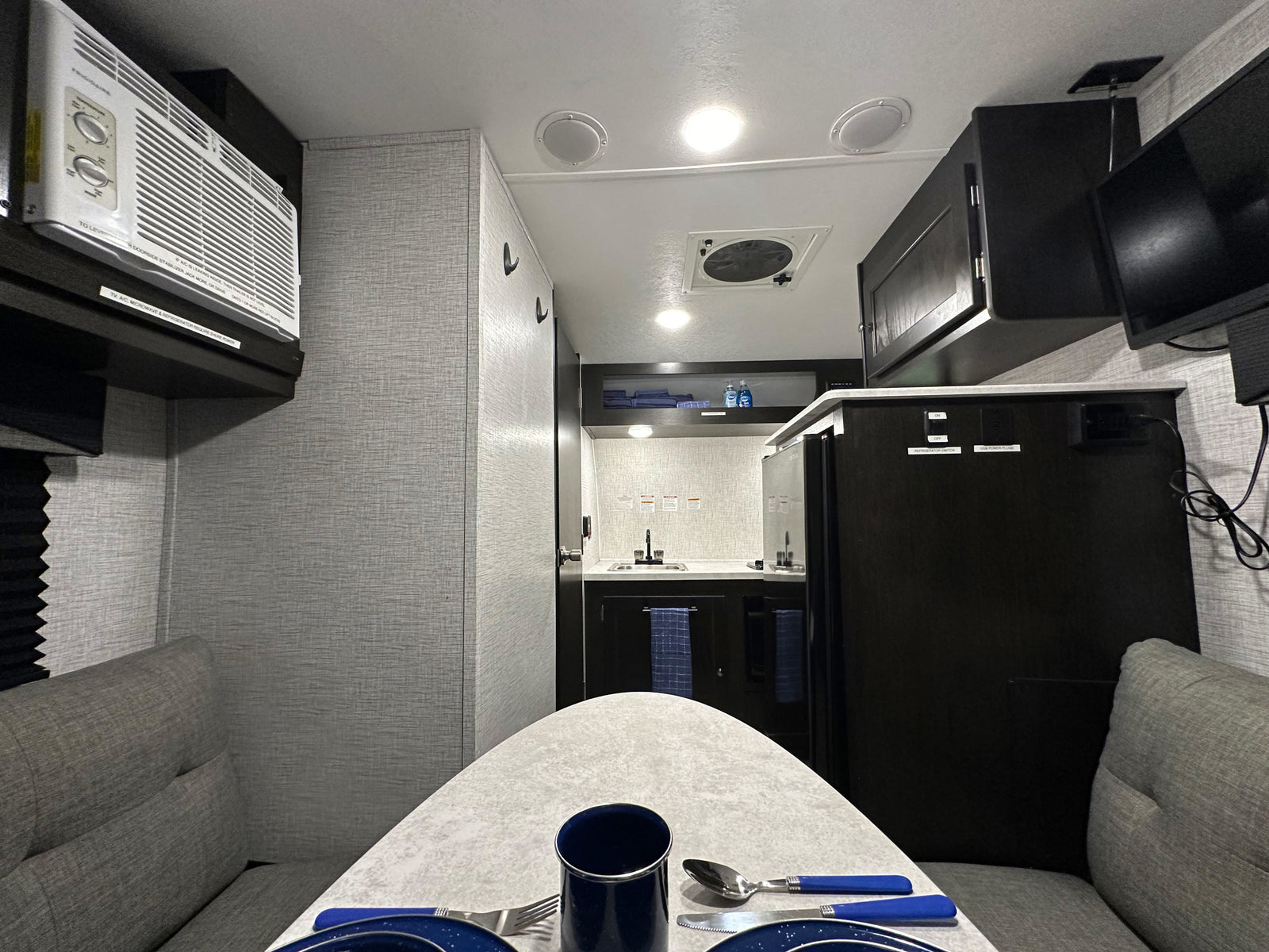 Inside a modern rv rental: dining table setup, compact kitchen, AC unit, and entertainment for a comfortable journey.