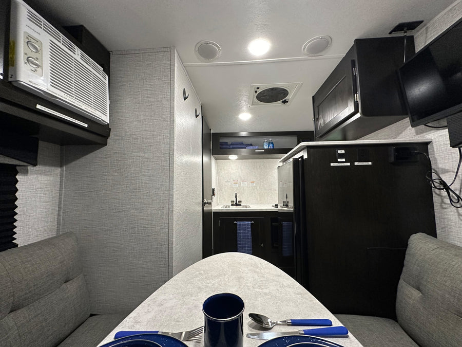 Inside a modern rv rental: dining table setup, compact kitchen, AC unit, and entertainment for a comfortable journey.