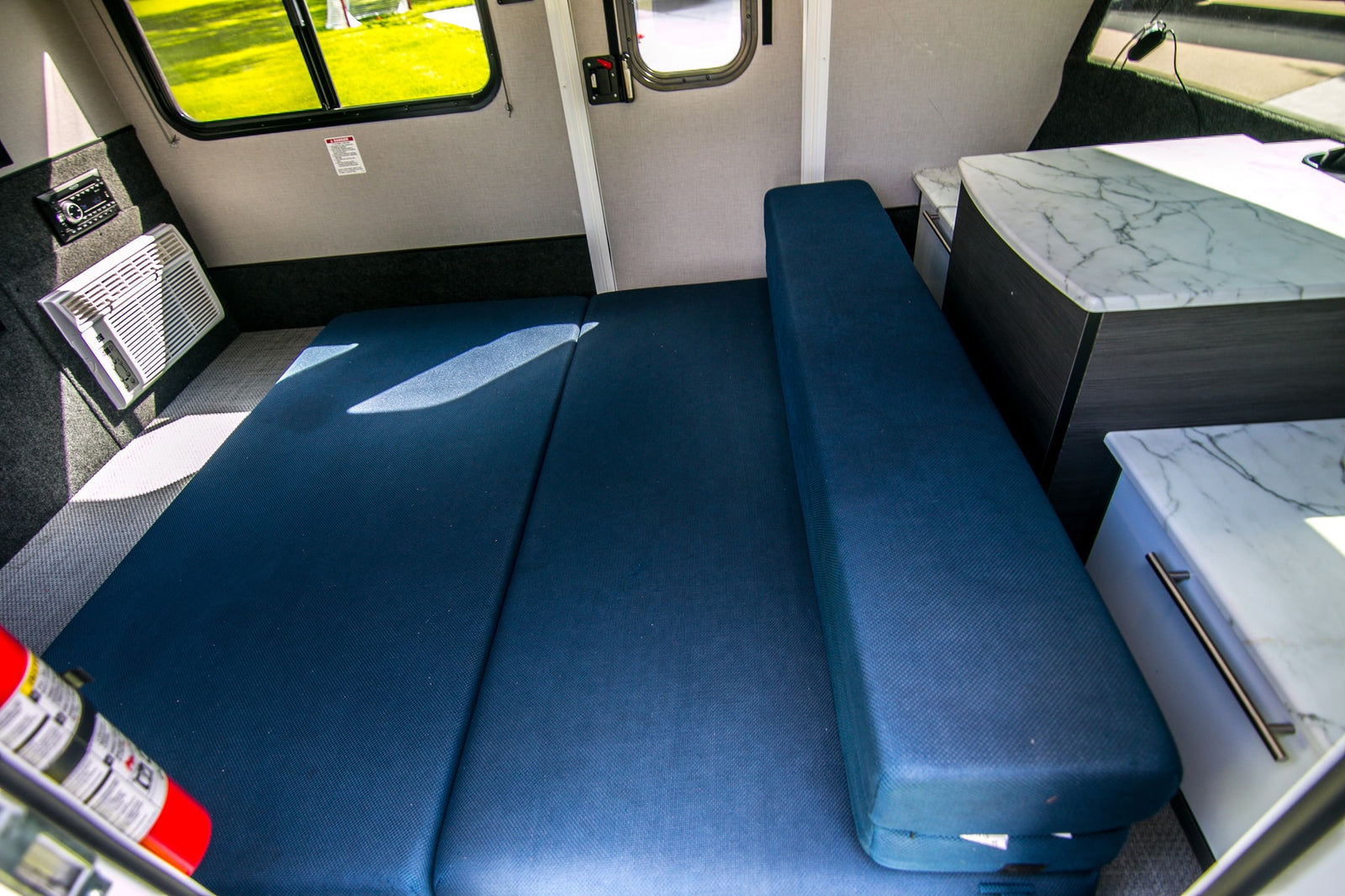 RV rental interior: blue convertible bed, AC, stereo, and stylish marble counters, perfect for compact living.