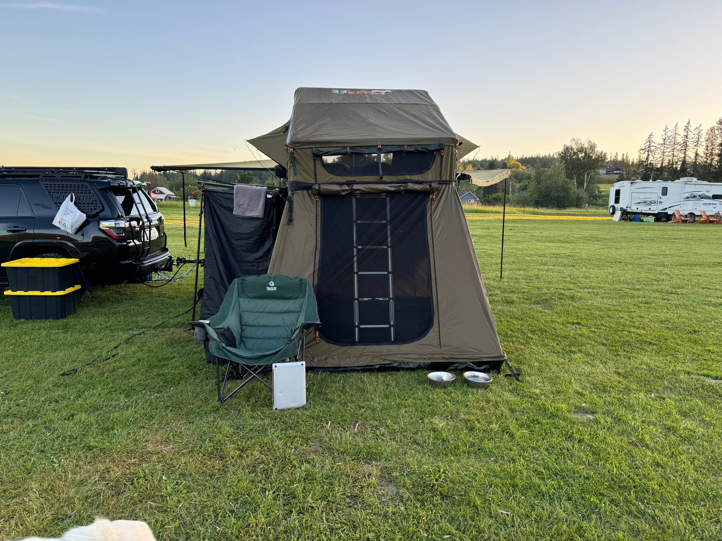 An overland camping setup featuring a roof top tent and SUV on a grassy field, near an RV rental, ready for outdoor adventure.