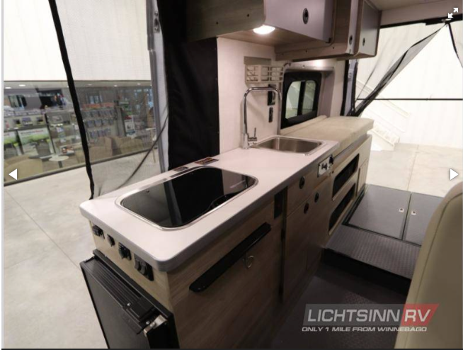 Step inside this RV rental! A compact interior boasts a full kitchen with sink/stovetop, fridge, & versatile living/sleeping zone.