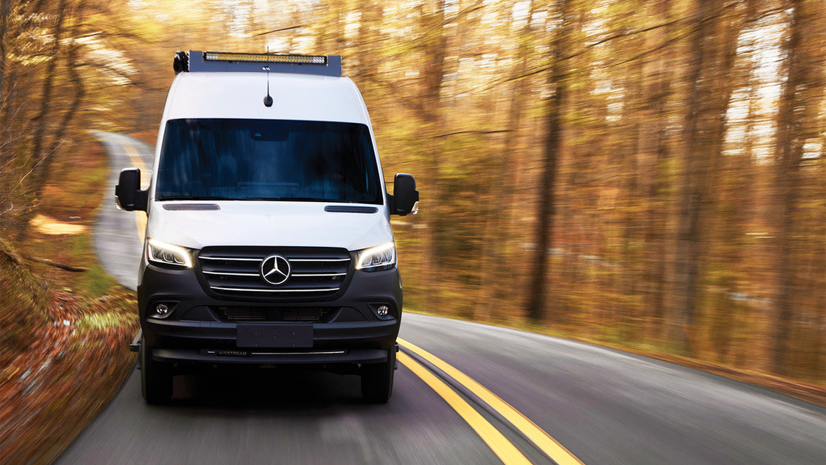 Experience autumn adventure! This white Mercedes Sprinter RV rental navigates a winding road through vibrant fall foliage.
