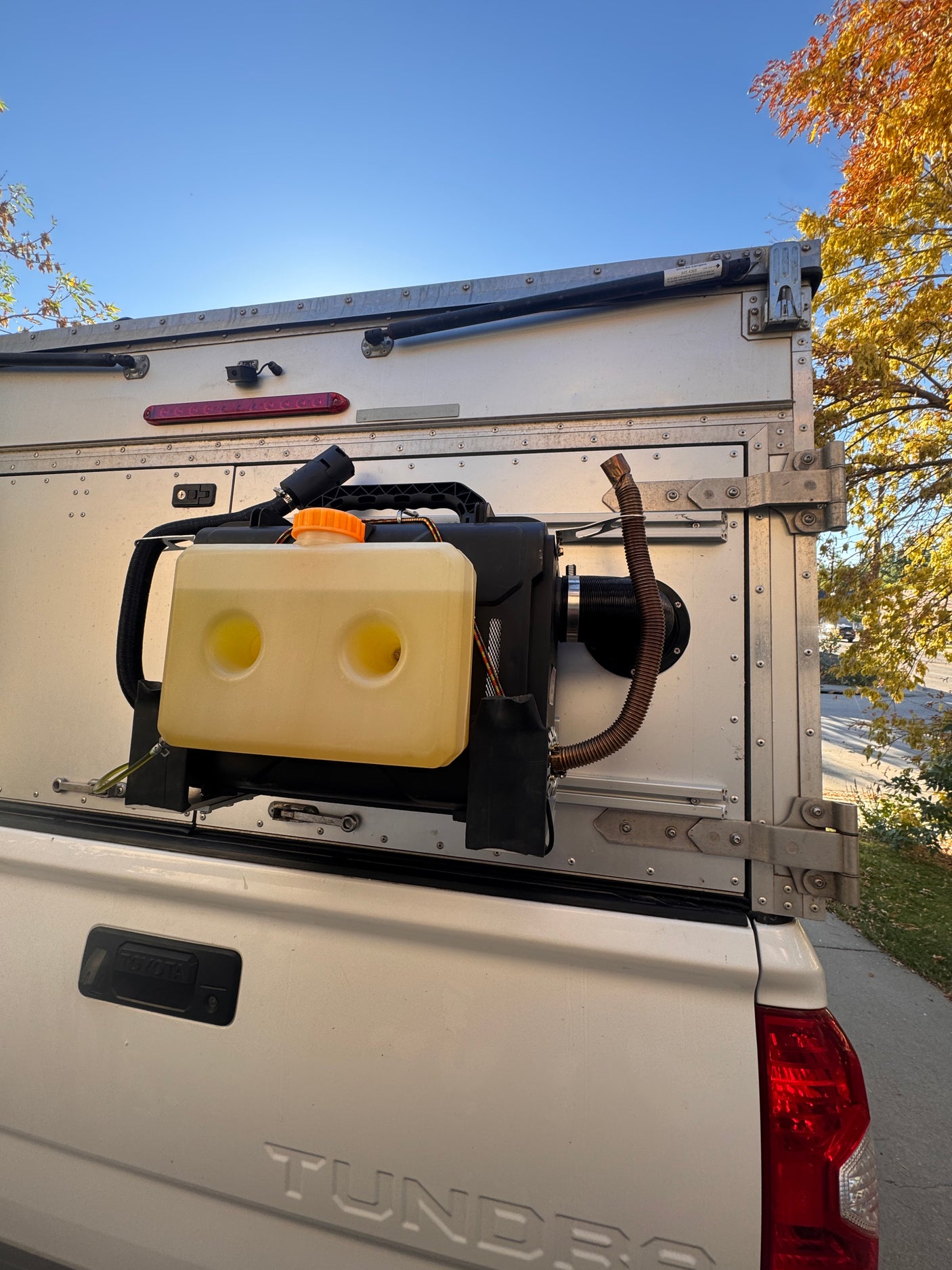 White Tundra truck camper with external diesel heater & tank, ready for cozy RV rental adventures.