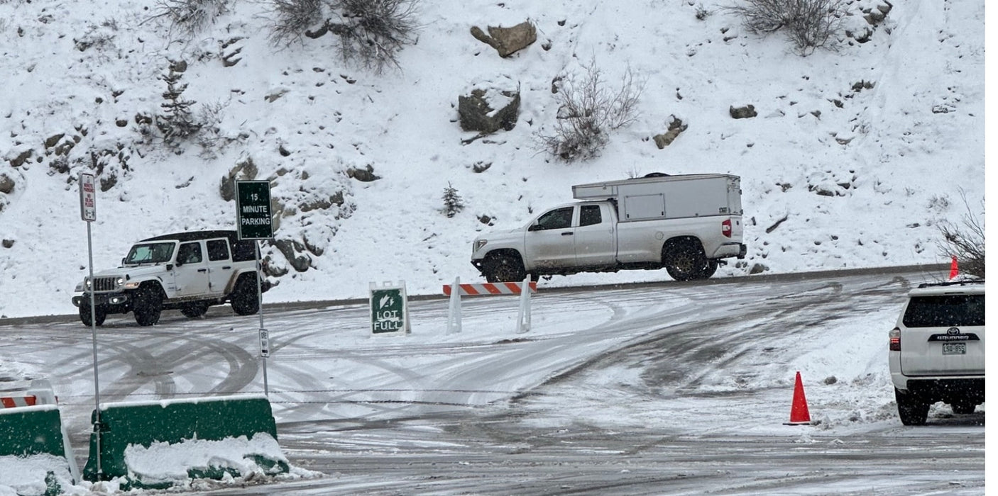Snowy mountain parking: Jeep, pickup with camper, SUV, & "Lot Full" sign. Plan your rv rental winter adventure.