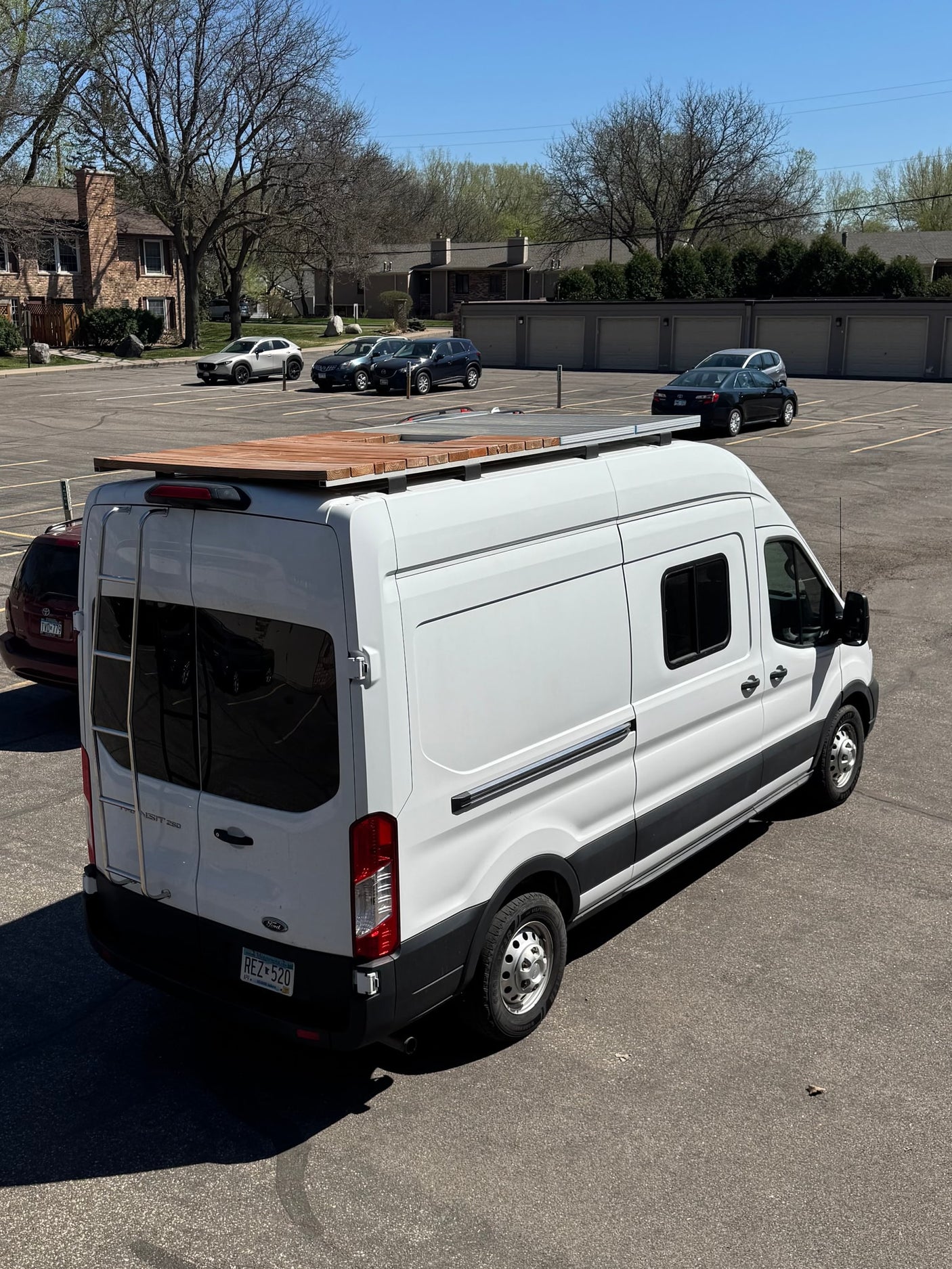 A white Ford Transit camper van, equipped with a roof deck and solar panels, visible in a parking lot. Ideal for rv rental adventures.