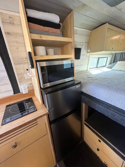 Cozy rv rental interior: compact kitchen (induction cooktop, microwave, fridge), bed, and built-in storage.