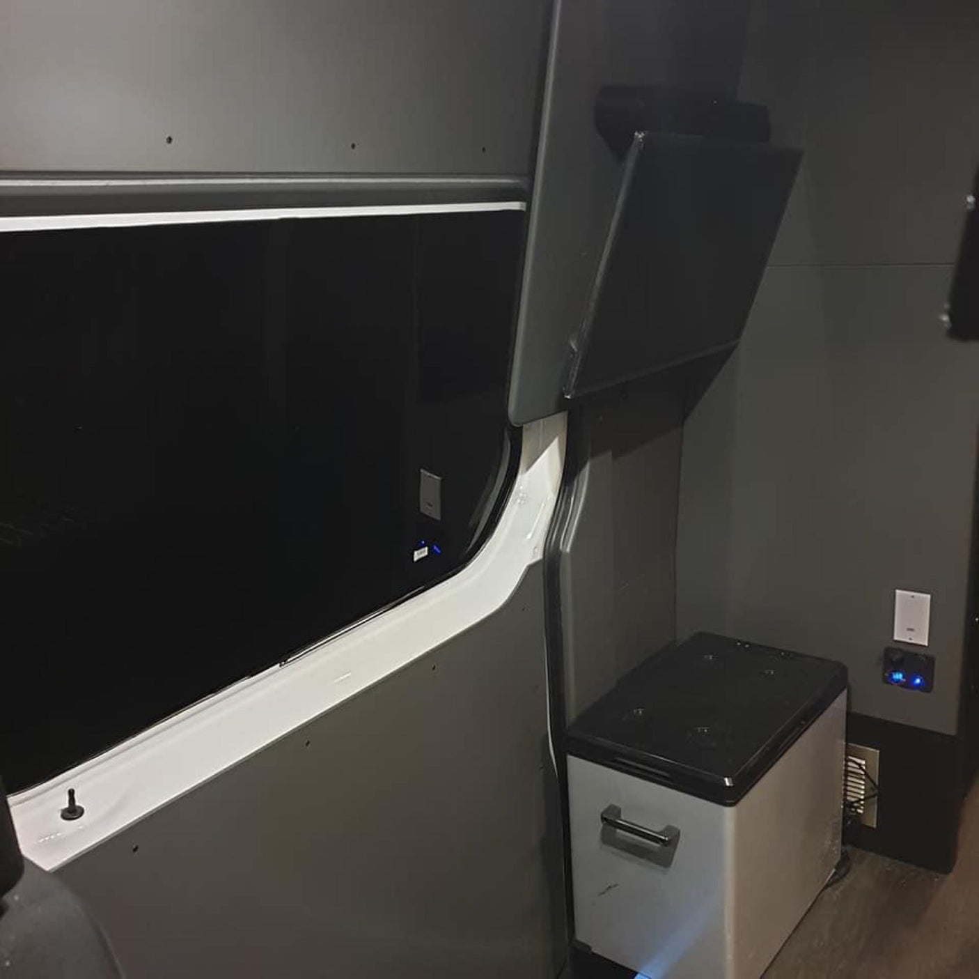RV rental van conversion: Dark gray interior with large window, portable fridge, power outlets, and open overhead storage.