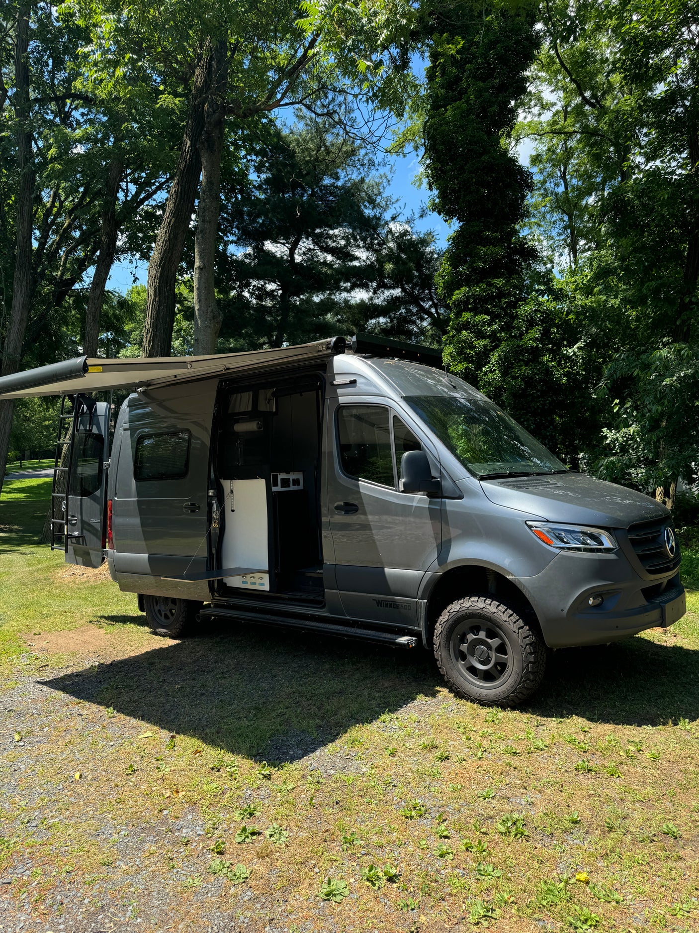 This rugged gray Mercedes-Benz Sprinter campervan rv rental is parked with its awning extended and side door open, ready for adventure.