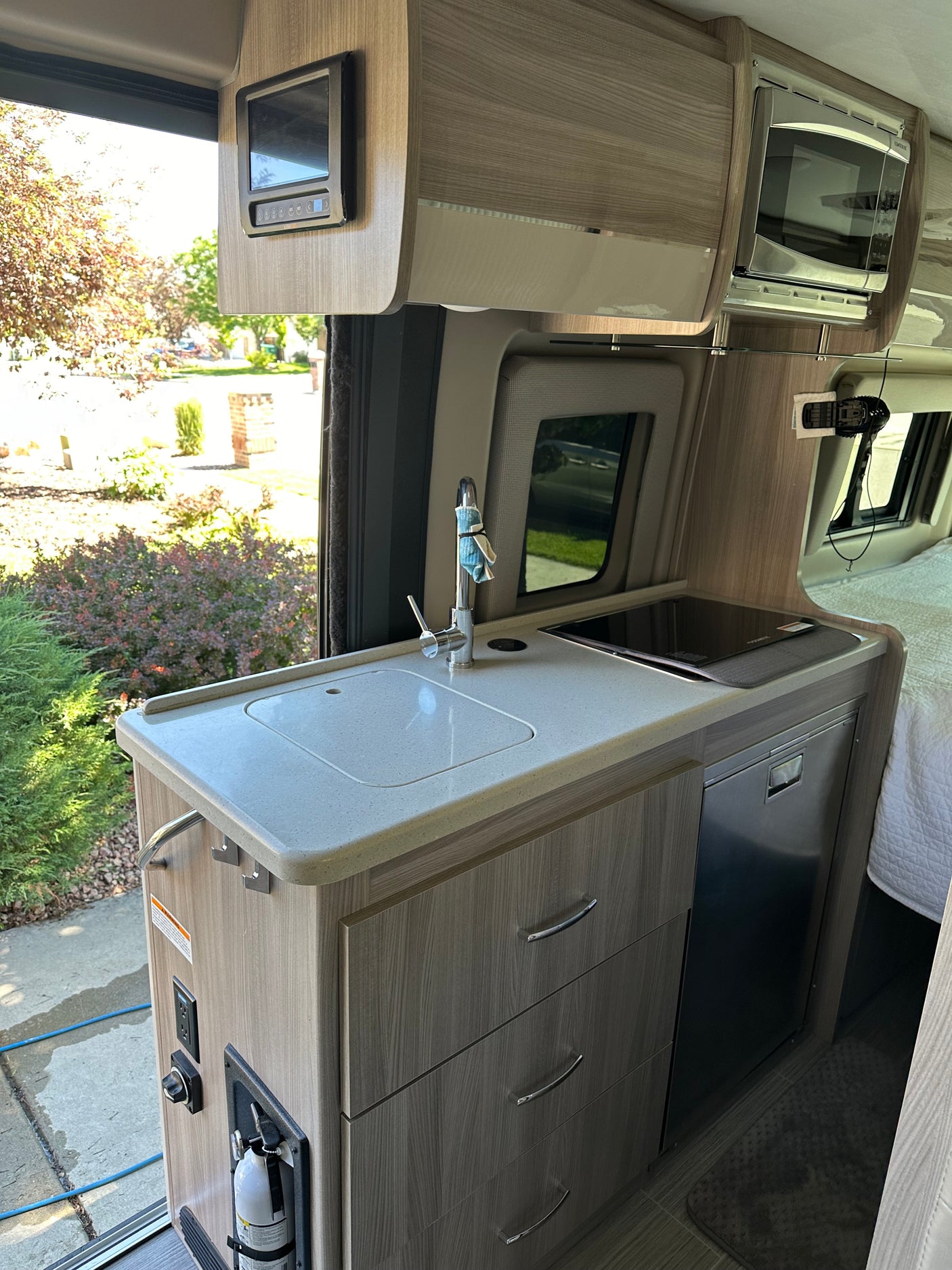 Inside an RV rental: a modern kitchenette with a bright counter, sink, induction cooktop, fridge, and overhead microwave.