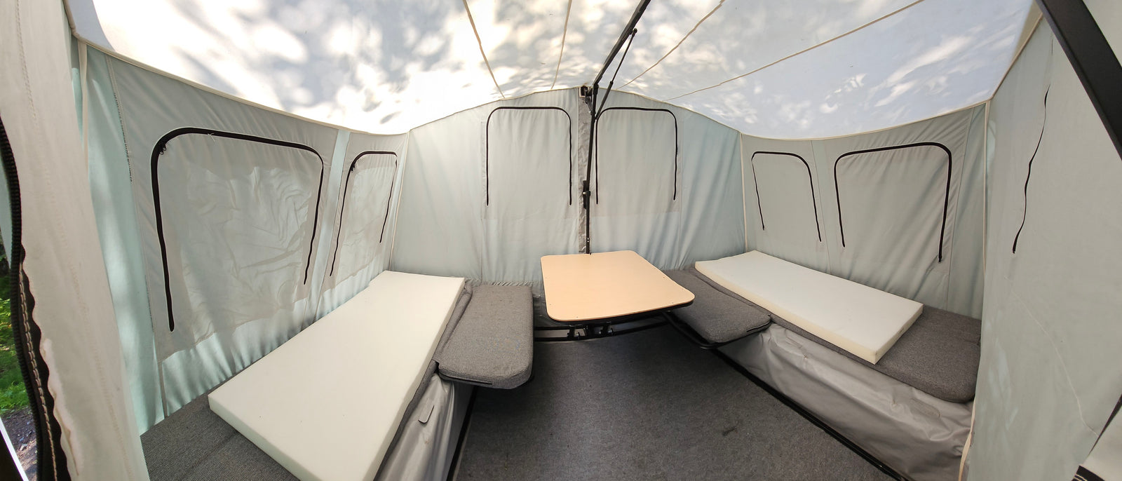 This RV rental's pop-up camper interior features bench beds, a center table, and light tent-style walls.