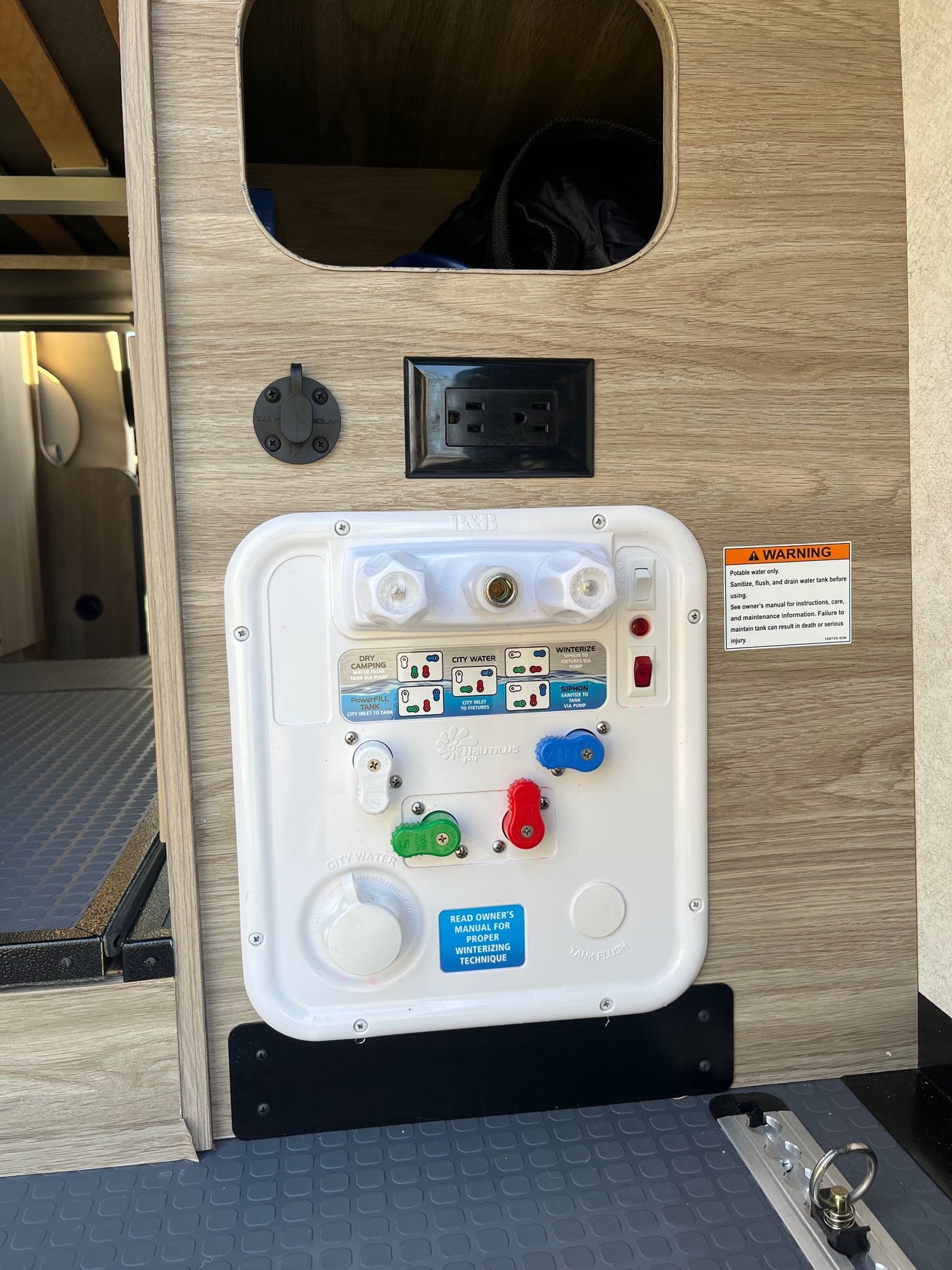 This RV rental utility panel features diverse water connections, an AC outlet, a ZAMP solar port, and a safety warning label for water system management.