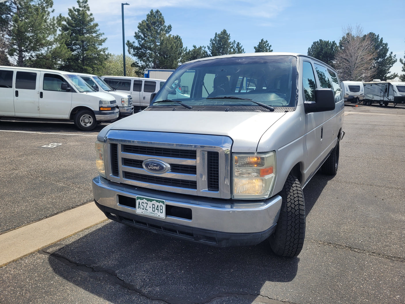 Silver Colorado Ford van at an RV rental lot, with other vans and RVs visible in the background.