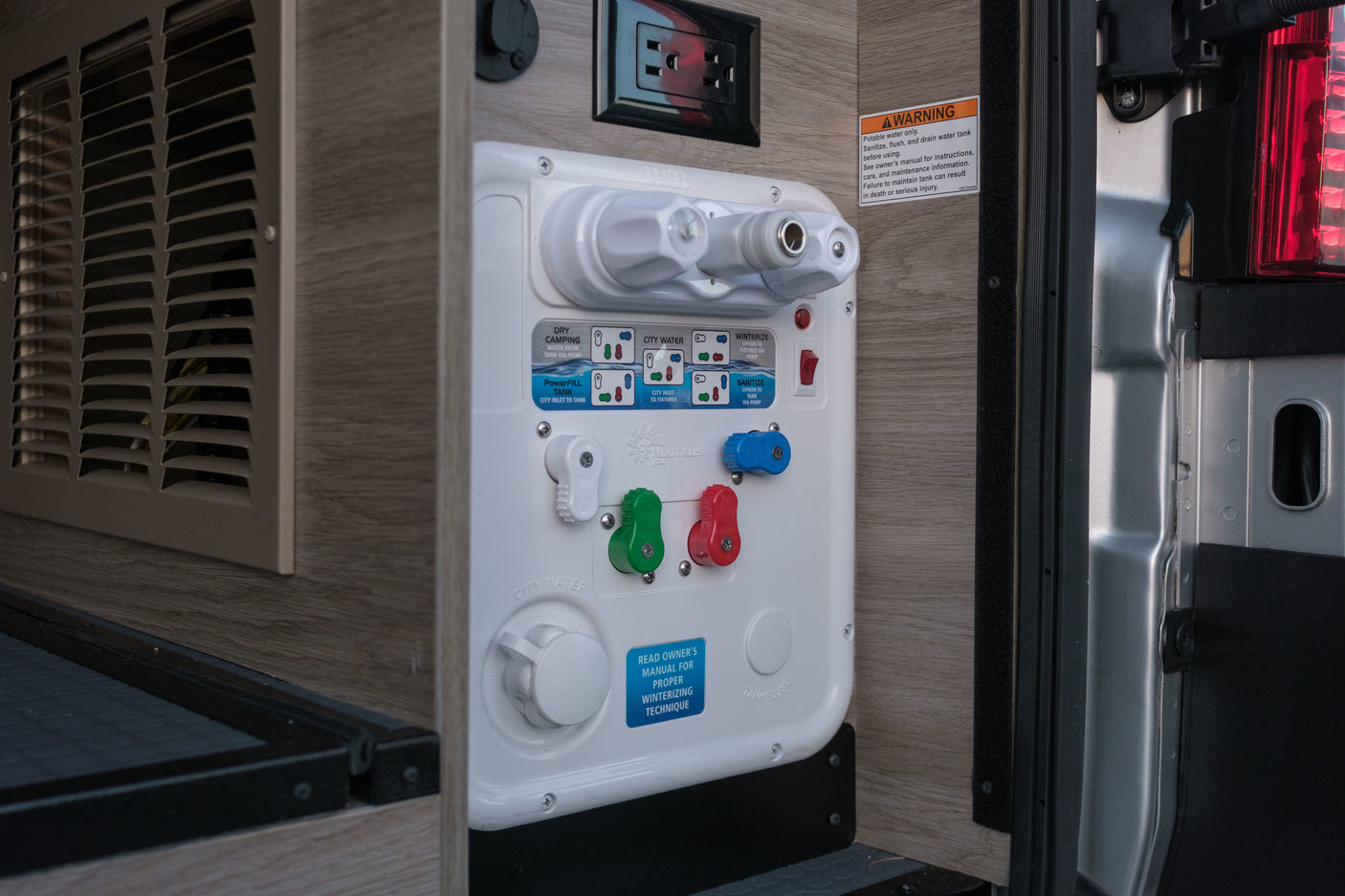 Essential RV rental utility panel: a multi-mode water system with valves, warning, & power outlet for camper operation.