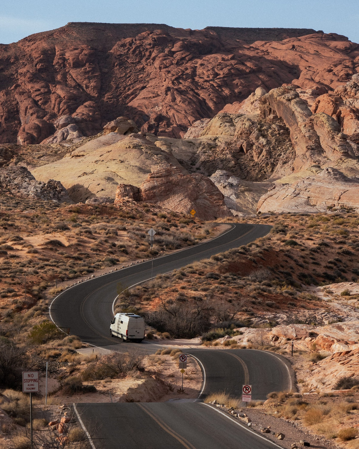 An RV rental navigates a winding desert road, surrounded by majestic red and tan rock formations under a clear sky. — photo 5