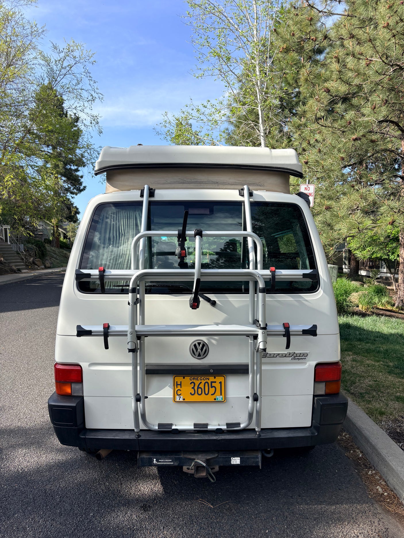 Rear view of a white VW EuroVan camper, an ideal RV rental, with a bike rack & Oregon plate. Parked outside on a sunny day.