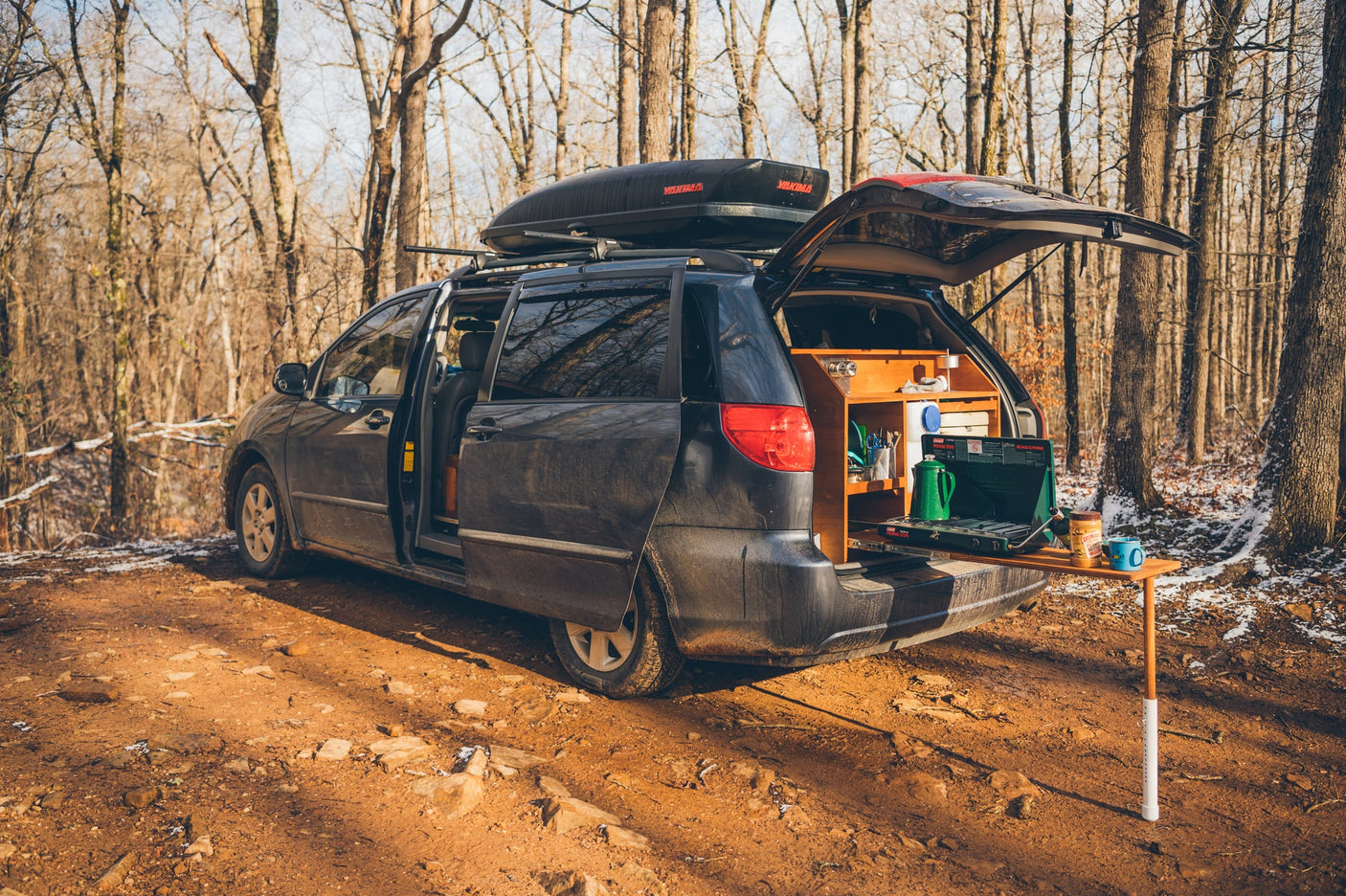 This customized minivan RV rental has its rear kitchen open in a winter forest