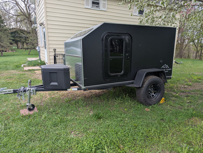 Black teardrop camper trailer, ideal for an RV rental adventure. Parked in a grassy yard, ready for camping trips.