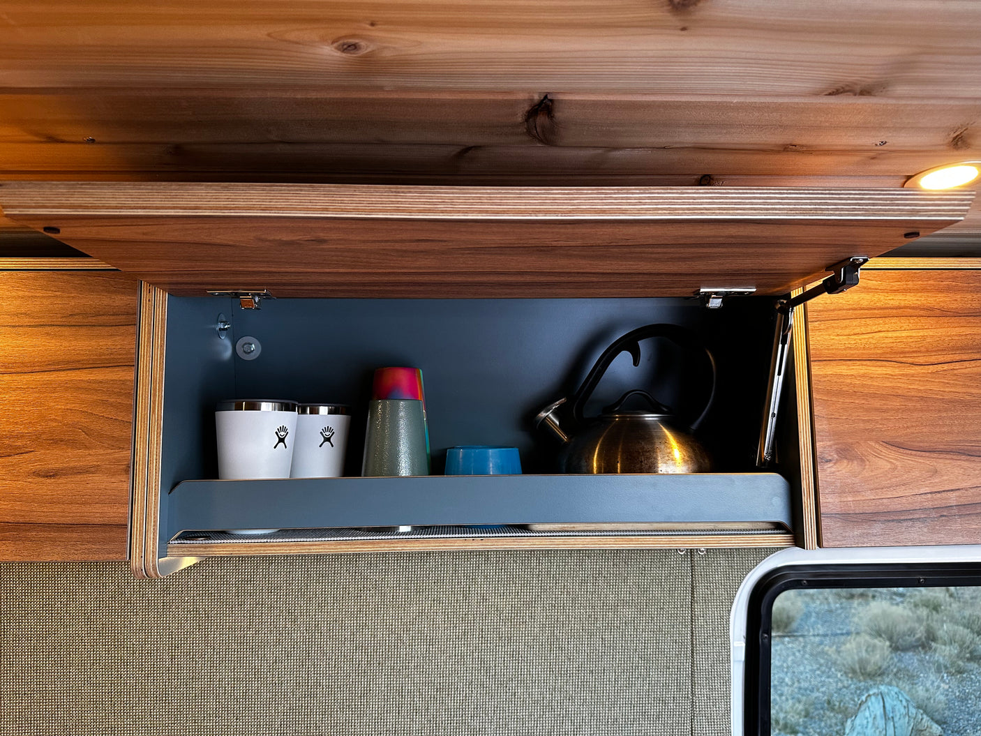 Organized RV rental kitchen cabinet: open, with a shiny kettle, white cups, and colorful bowls, ready for travel or camping.