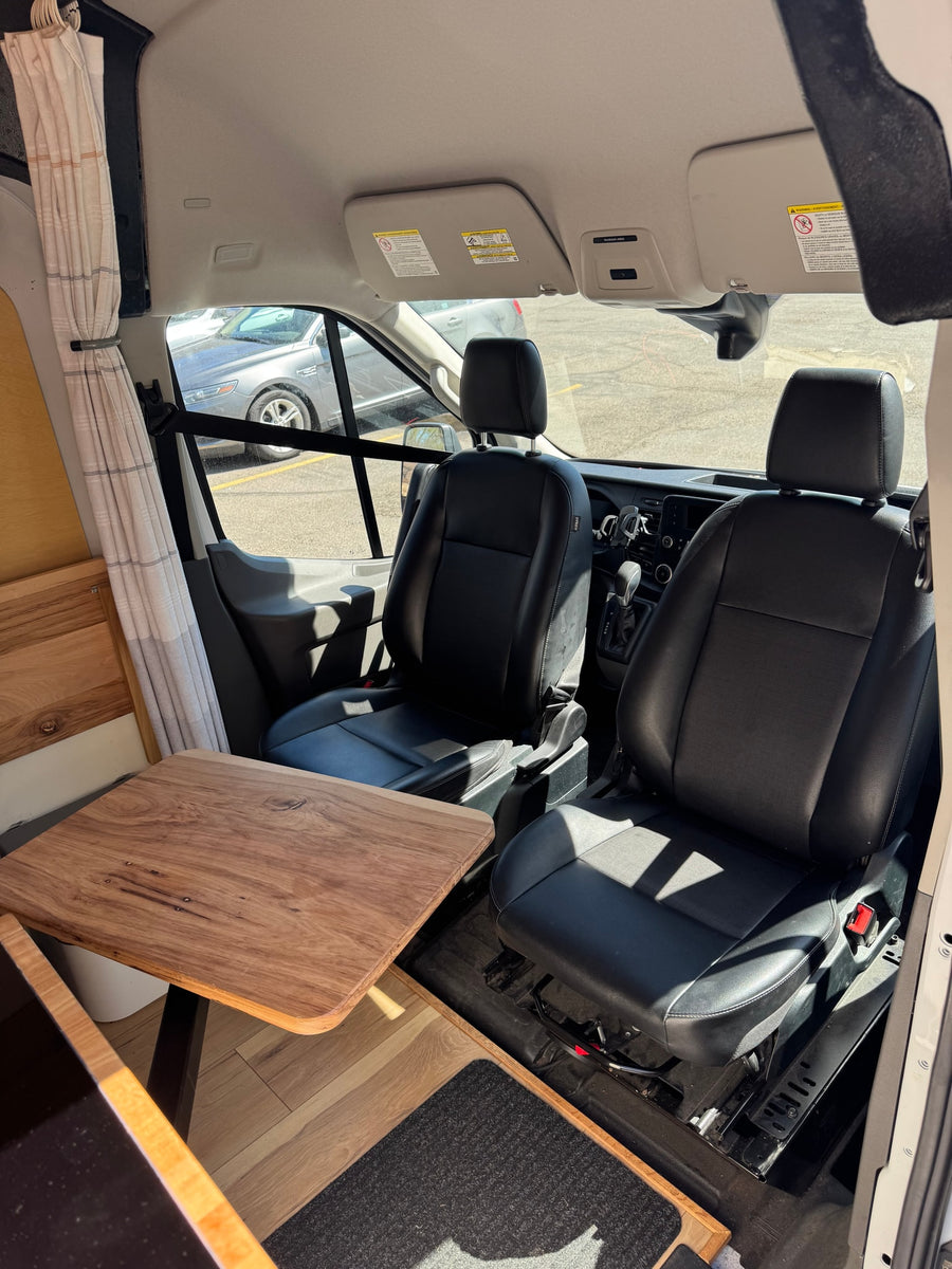 RV rental's front cabin: black leather seats, custom wooden table, and privacy curtains for mobile living.