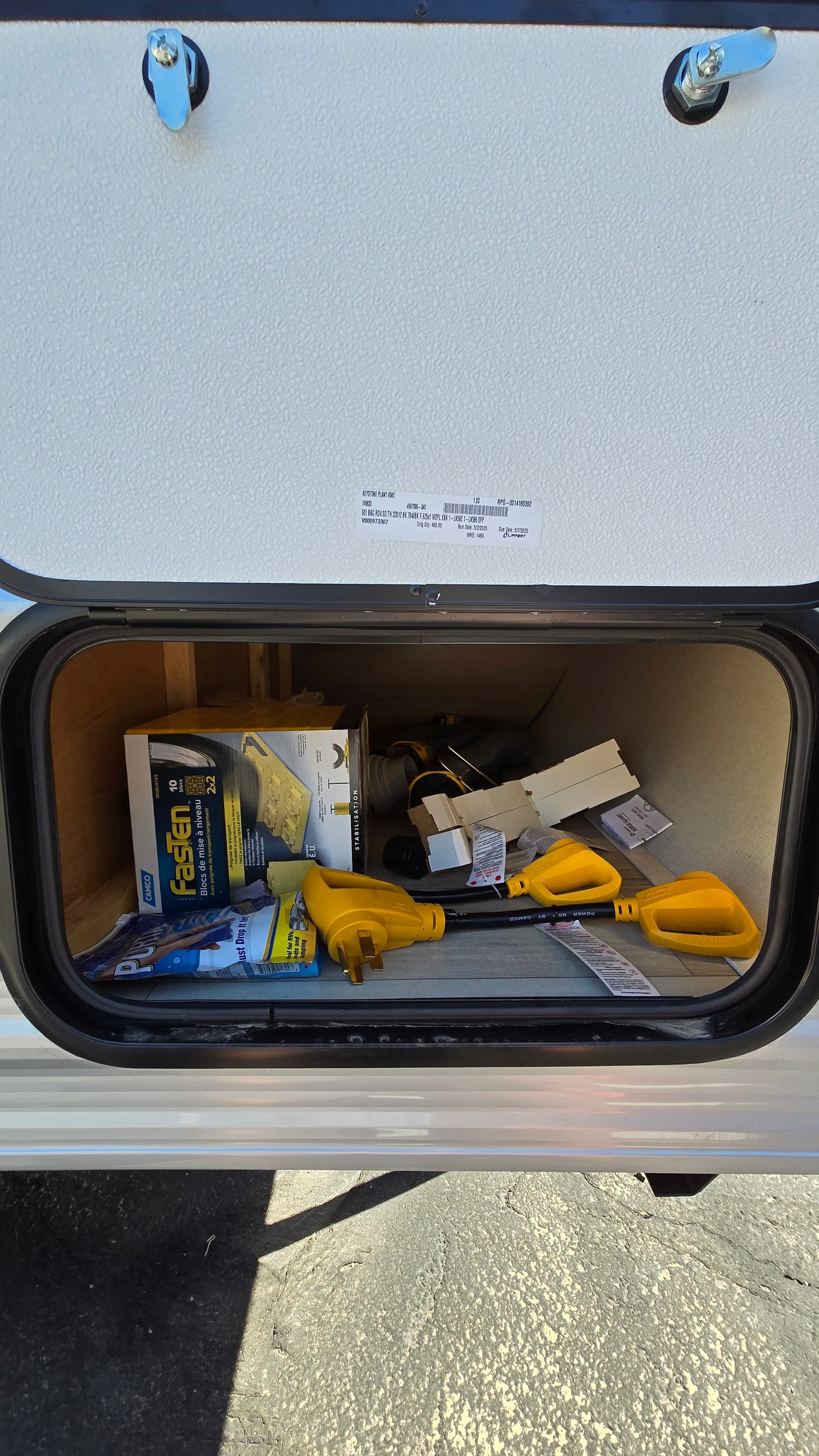 Open RV rental storage compartment reveals essential camping gear: power adapters, leveling blocks, and other RV accessories.