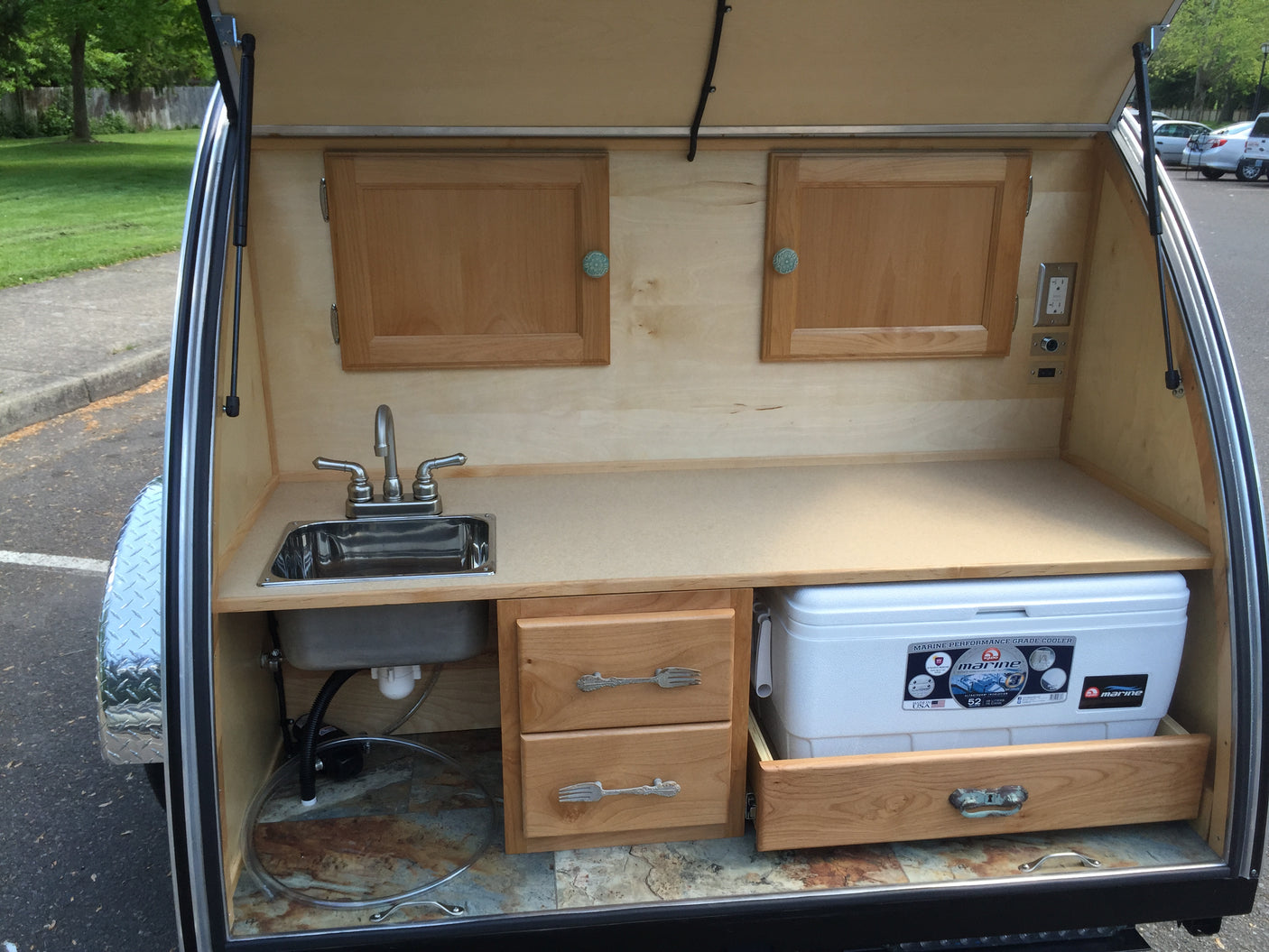 Rear kitchen galley of an RV rental: features a sink, faucet, cooler on a pull-out drawer, and wooden storage.
