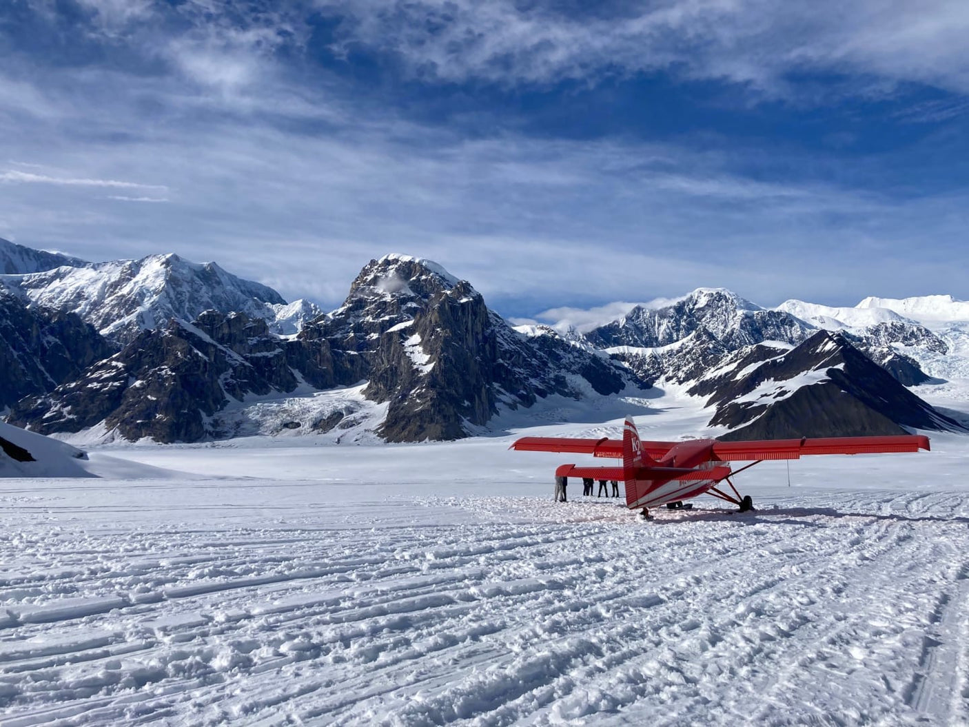 Red plane on a vast snowy glacier, majestic mountains behind. People board for a unique adventure, unlike any RV rental.