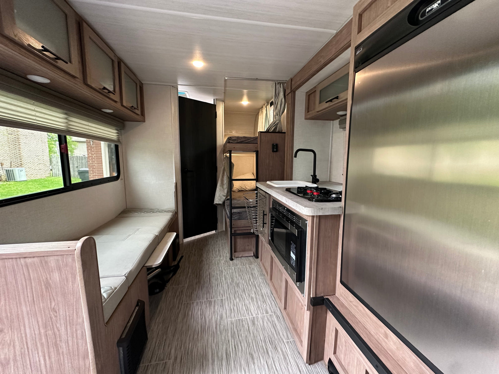 View of an RV rental's functional interior: kitchen, fridge, bunk beds, and bench seating.