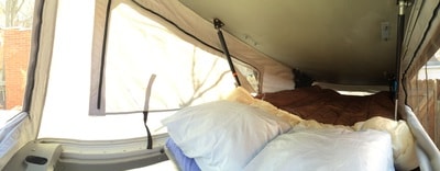 Cozy sleeping area inside an RV rental pop-up camper, featuring a bed with pillows and fabric walls.
