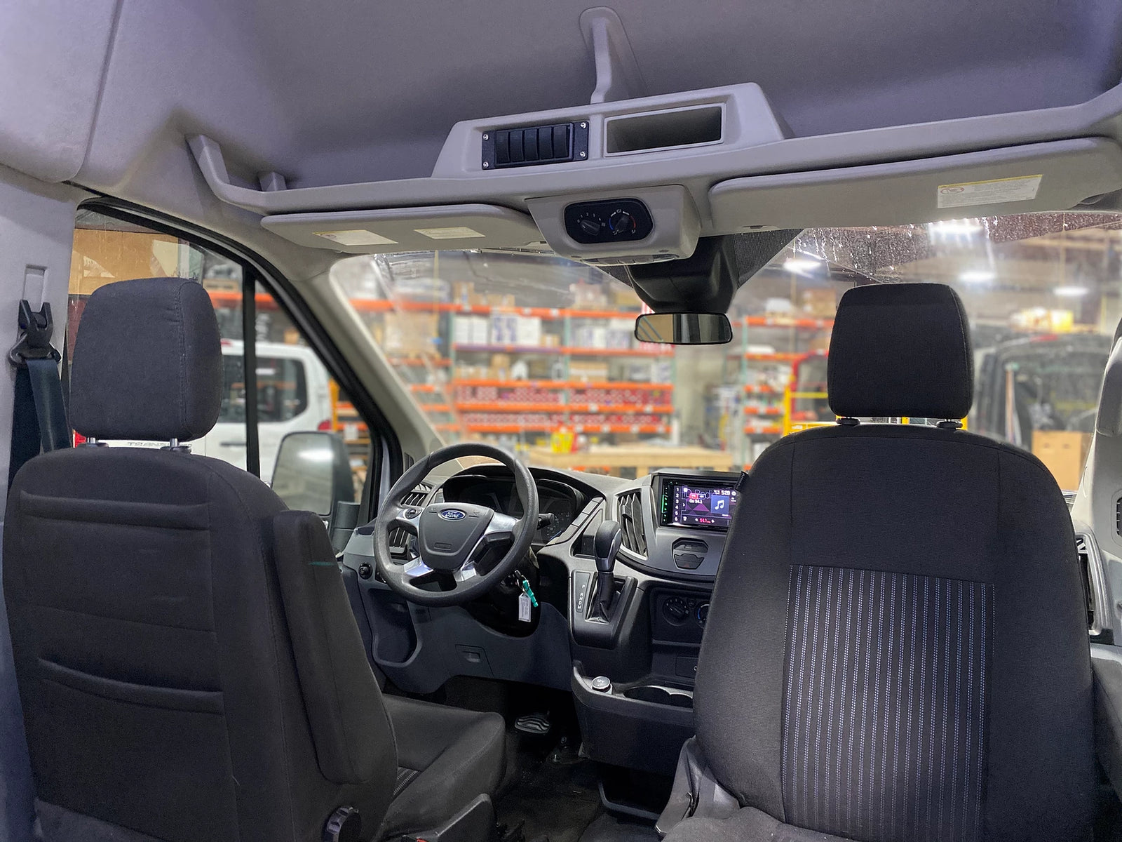 Spacious Ford Transit RV rental interior, from rear. Features front seats, dashboard, media, and overhead controls.