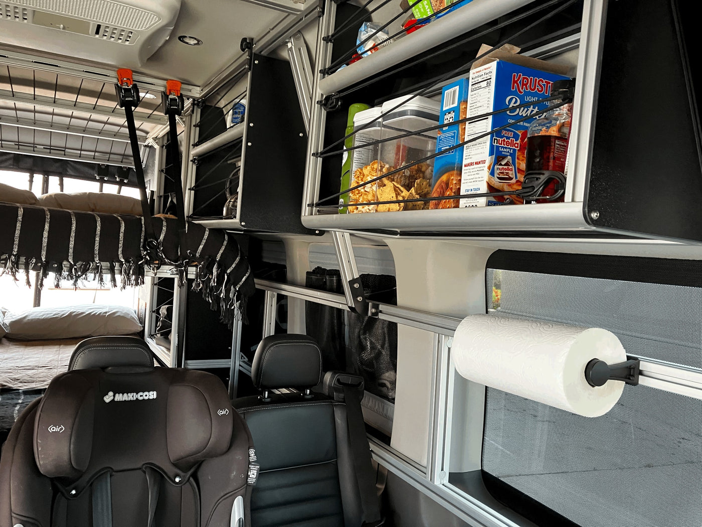 RV rental interior: bunk beds, child car seat, overhead shelving with groceries, and a paper towel holder. Designed for family travel. — photo 19