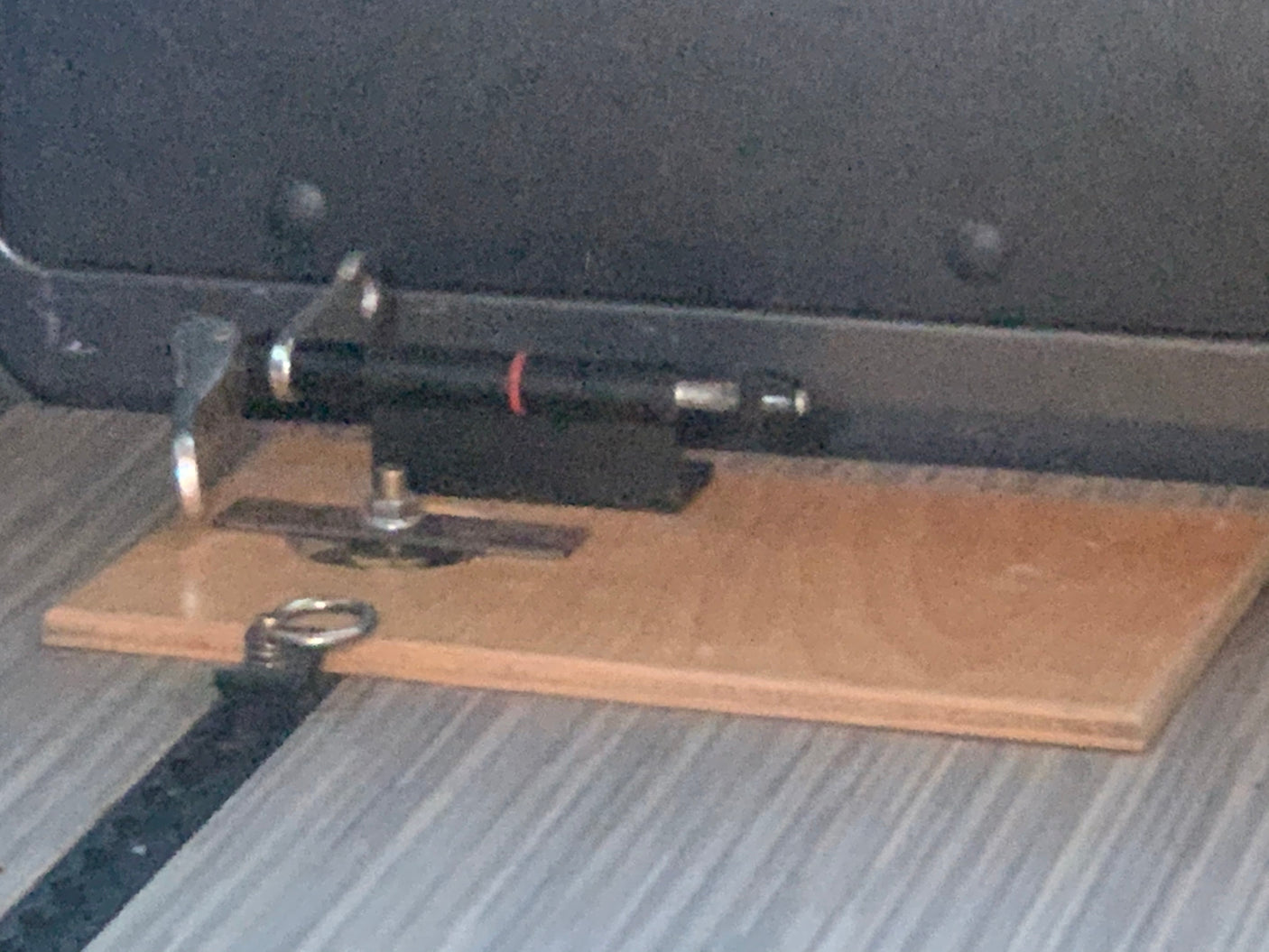 A black pen-like object is custom-mounted on a wooden base, likely for an RV rental interior, showing a clever storage solution.