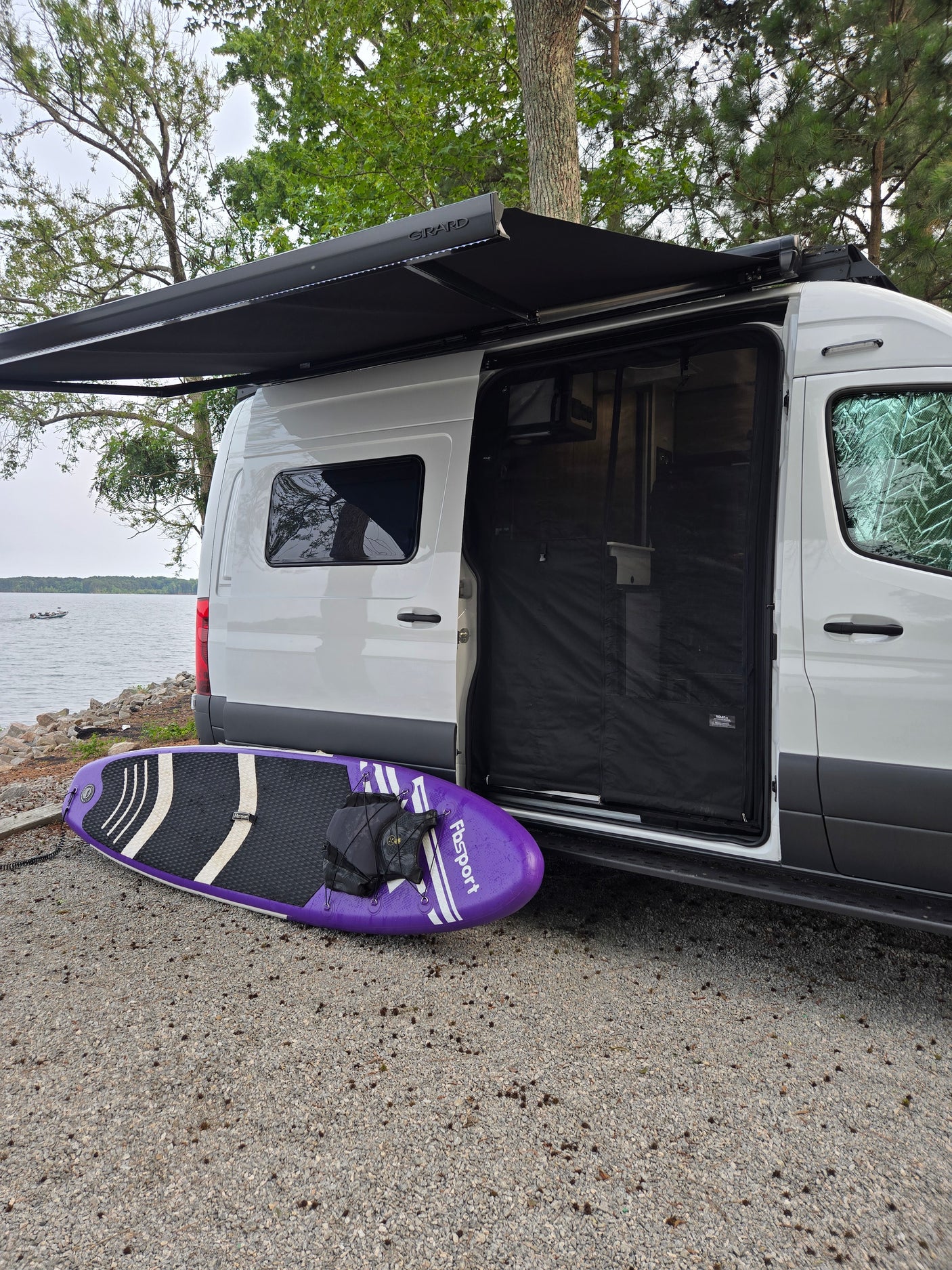 Experience an RV rental: Van life by the lake, with a paddleboard and extended awning ready for adventure.