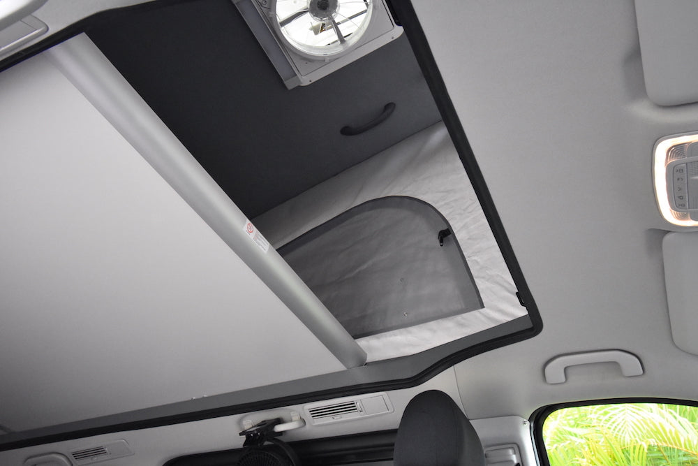 This RV rental interior shows a pop-top roof extended, revealing an overhead bed with a fan. Clear and spacious.