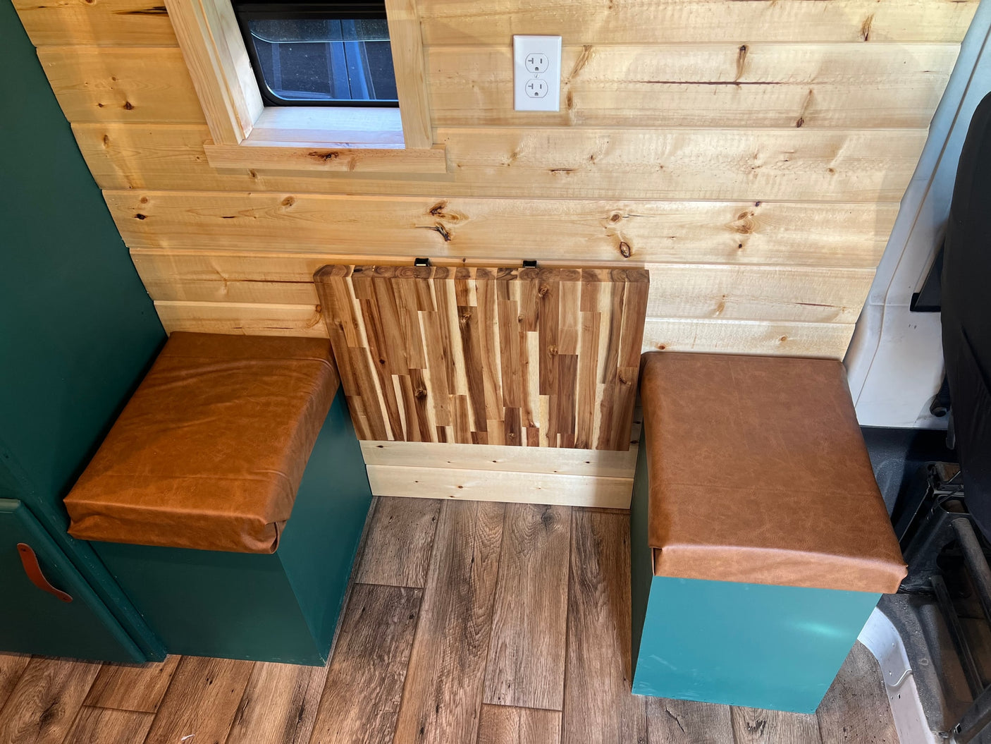 RV rental: Custom wood interior with teal storage benches, brown cushions, and a versatile wooden table, perfect for van life comfort.