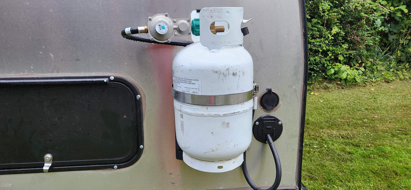 Side of an RV rental showing a propane tank with regulator and shore power inlet for outdoor living.