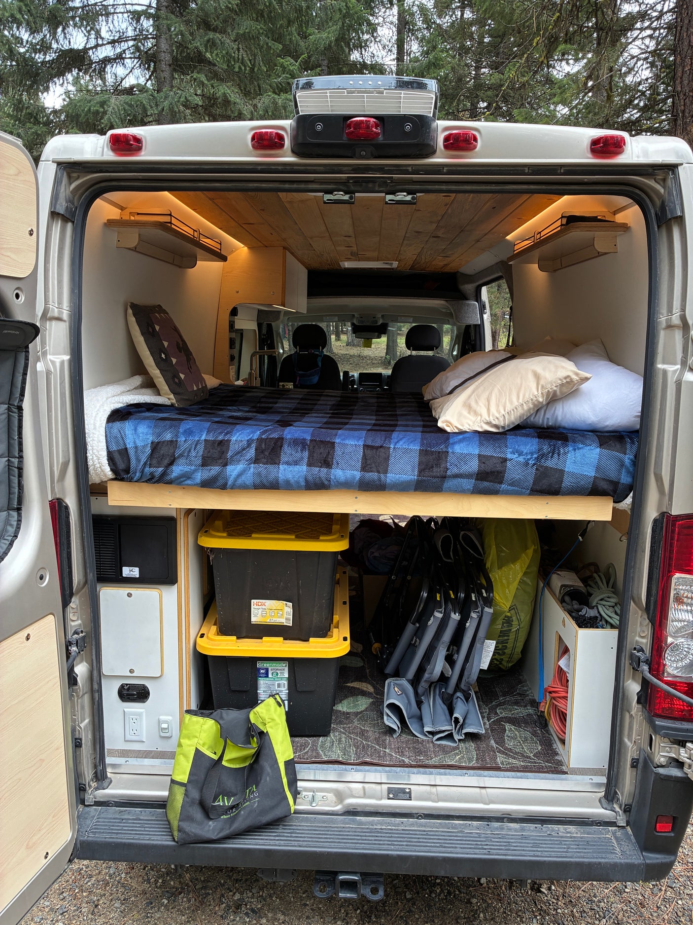 Open rear view of an rv rental camper, revealing a cozy bed with a blue plaid blanket, ample storage, and interior details.