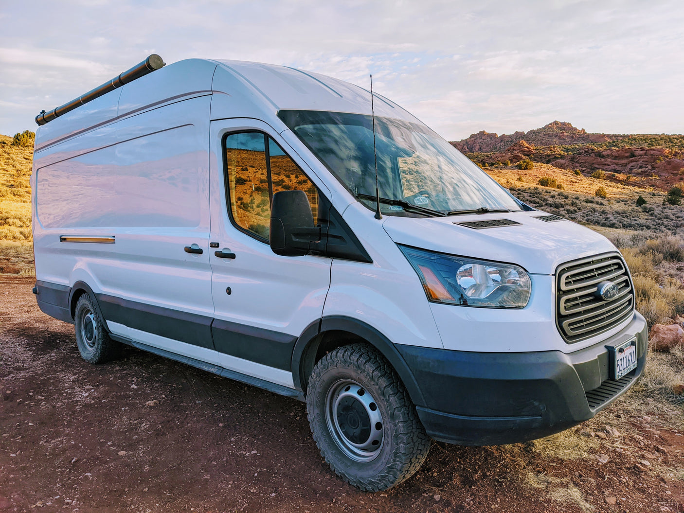 White Ford Transit camper van parked on a dirt road in a desert landscape. Perfect for an RV rental adventure!