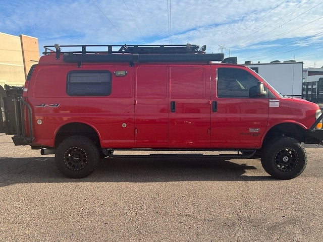 ideal for an RV rental adventure. Equipped with a roof rack and rear ladder.|Red lifted 4x4 adventure van with roof rack & off-road tires